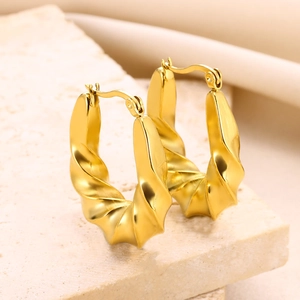 Detailed view of gold twisted hollow earrings on light beige textured stone base