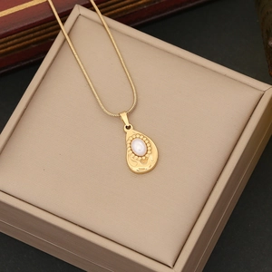 Detailed view of a gold teardrop pendant with white oval pearl on a cream jewelry box