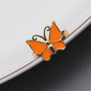 Detail showing an orange enamel butterfly adjustable ring on a white porcelain edge