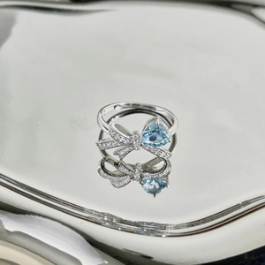 Macro shot of silver bow ring with blue heart zircon reflected on a metallic mirror surface