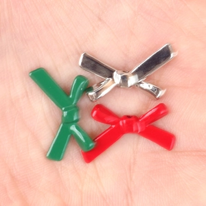 Minimalist alloy bow tie beads in silver, green, and red on palm for size scale