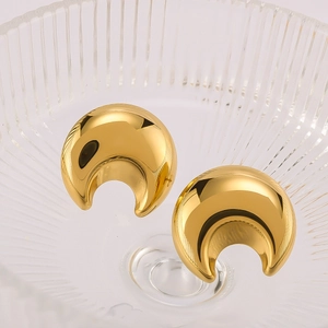 Polished gold crescent moon titanium steel earrings displayed on a glass tray