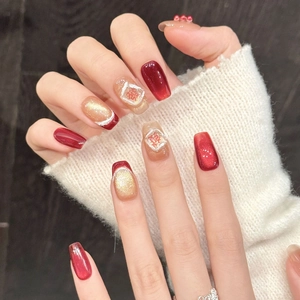 Primer plano de uñas postizas rojas y doradas con caracteres xi y perlas blancas