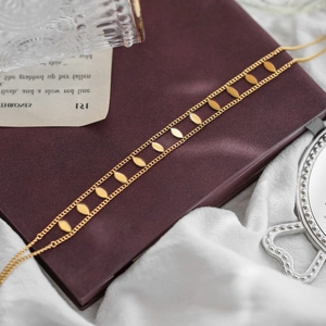 Elegant 18K gold double-layer necklace with oval leaf pendants on a red leather diary