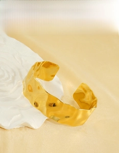 Detail of 18K gold-plated hammered texture cuff bracelet on elegant silk background