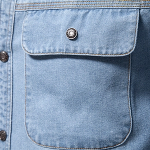 Détail de chemise en jean bleu clair avec poche à rabat, bouton et double couture