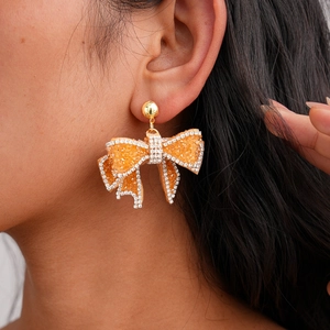 Bowknot fringe drop earrings with orange resin and sparkling rhinestones worn by a woman