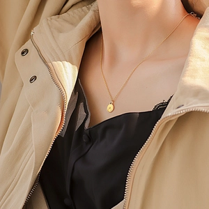 Minimalist gold coin necklace with star pendant worn on model over a stylish coat