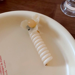 Gros plan d'une pince à cheveux spirale fleurie tons crème et jaune sur plat céramique