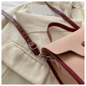 Close-up of pink and burgundy textured leather crossbody bag with white stitching detail