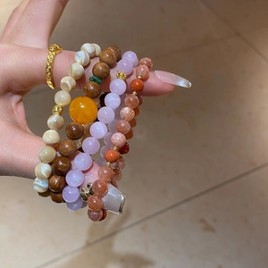Stacked beaded bracelets with natural stones, tiger eye, and gold bow charm on wrist