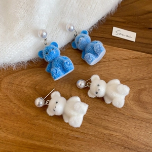 Detail of blue and white flocked bear earrings with pearl studs on a wooden surface