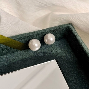 Close-up of elegant round white pearl earrings on a dark green velvet display box