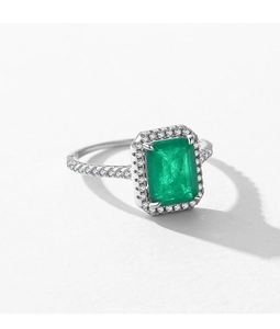 Macro shot of silver ring with emerald-cut green gemstone and halo diamonds
