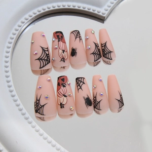 Halloween press-on nails featuring orange pumpkin, black spider web, and rhinestones