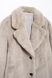 Detail view of the soft faux fur texture and collar label on the beige winter coat