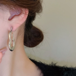 Detail of silver irregular flame-shaped stud earrings showing a fluid liquid metal texture