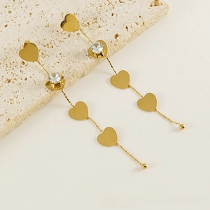 Macro view of long 18K gold tassels earrings with heart shapes and zircon stones