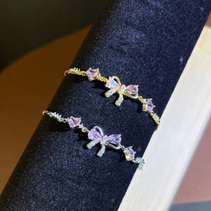 Close-up of gold and silver bow bracelets with pink zircon hearts on a display