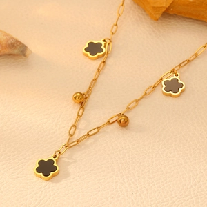 Detail of gold paperclip chain necklace with black clover motifs and small metal beads