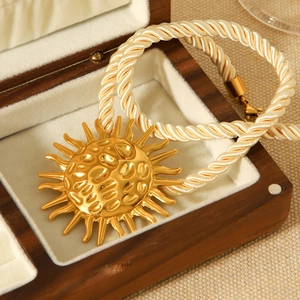 Hammered gold sun pendant necklace with braided rope chain on jewelry display box