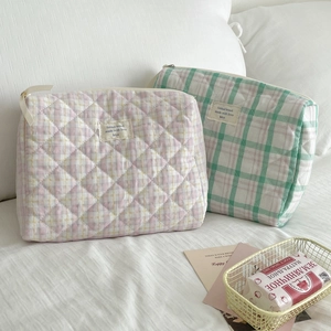 Detail of quilted plaid cosmetic bags with zipper closure and brand label in pastel colors