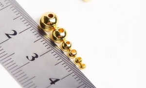 Macro view of 18k gold plated round beads shown with a ruler for size measurement