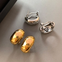 Macro shot of minimalist gold and silver bean-shaped earrings with engraved details