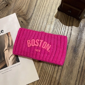 Détail macro du bandeau tricoté rose avec texte BOSTON 1630 en relief sur bois sombre