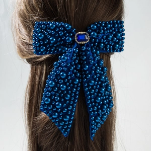 Detail of dark blue bow hair clip with pearls and crystal gemstone on brown hair