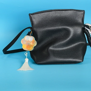 Detail of black crossbody bag with iridescent cat paw charm and white tassel fringe