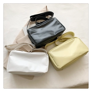 Three minimalist soft leather tote bags in black, white, and cream on a beige blazer