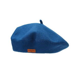 Navy blue wool beret with a brown leather logo tag displayed on a white background