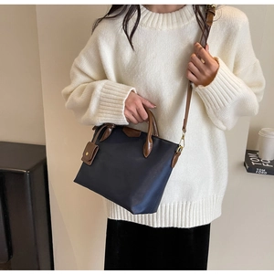 Detail of navy nylon bucket bag with brown leather strap worn by model in white sweater