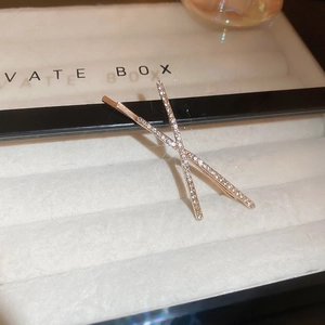 Detail of rose gold X-shaped hair clip with shimmering pavé rhinestones in a gift box