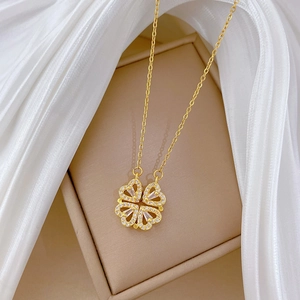 Close-up of golden four-leaf clover necklace with crystals on beige silk background