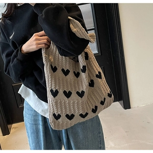 Vista de hombro de un bolso tote de punto beige con patrones de corazones negros en modelo