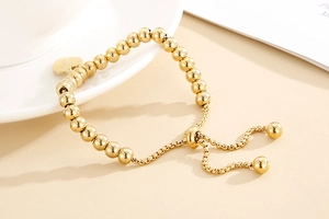 Detail of adjustable golden stainless steel beaded bracelet with heart charm and slider clasp