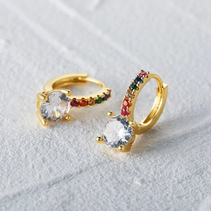 Macro detail of gold hoop earrings with a large clear zircon and rainbow gemstones