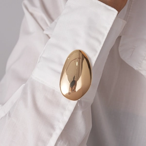 Detail of polished golden teardrop cufflink on a white shirt sleeve with mirror finish