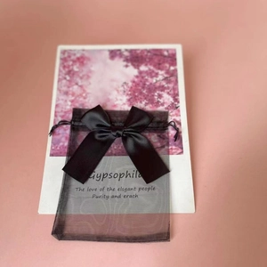 Detail of a black organza gift bag featuring a silky ribbon bow on a pink backdrop
