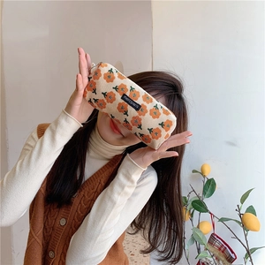 Detailed close-up of corduroy pencil case featuring orange floral patterns and woven label