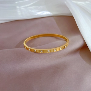 Close-up of golden stainless steel bangle with square set crystals on silk background