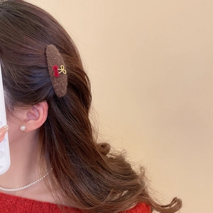 Detail of plush brown hair clip with red cherry and gold bow on wavy hair