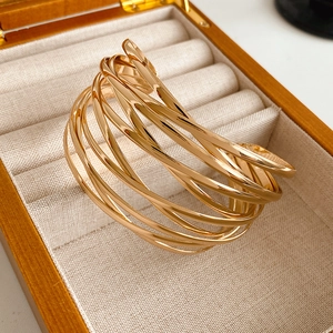 Close-up of a layered golden cross-over open bangle displayed in a wooden jewelry box