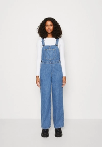 Detail of light blue denim overalls showing metal buckles and large front pocket design