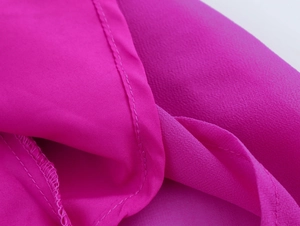 Dettaglio del tessuto in chiffon magenta con trama pieghettata e cuciture di precisione