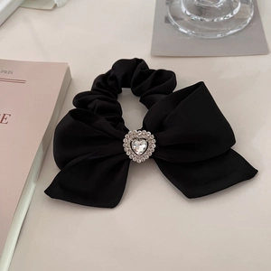 Detail of black satin bow scrunchie with a sparkling crystal heart centerpiece on warm desk