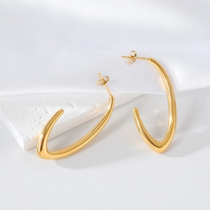 Close-up of golden irregular geometric hoop earrings on white marble and silk