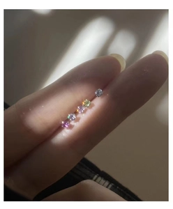 Close-up of tiny multi-colored cubic zirconia stud earrings held on a fingertip